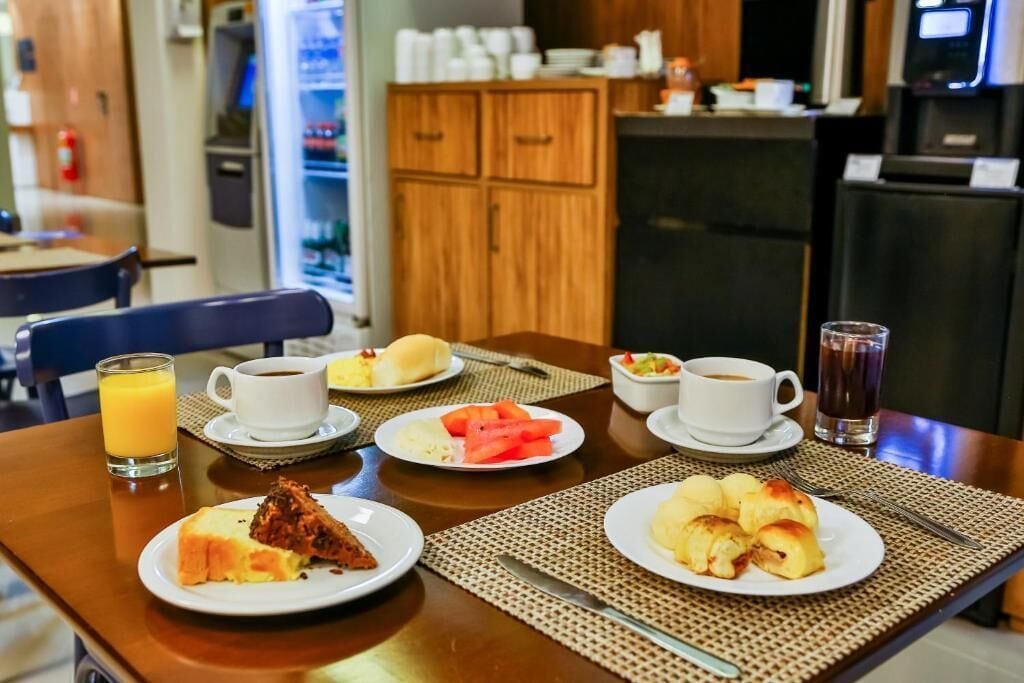 Una mesa de desayuno con platos de comida, tazas de café y un vaso de jugo.