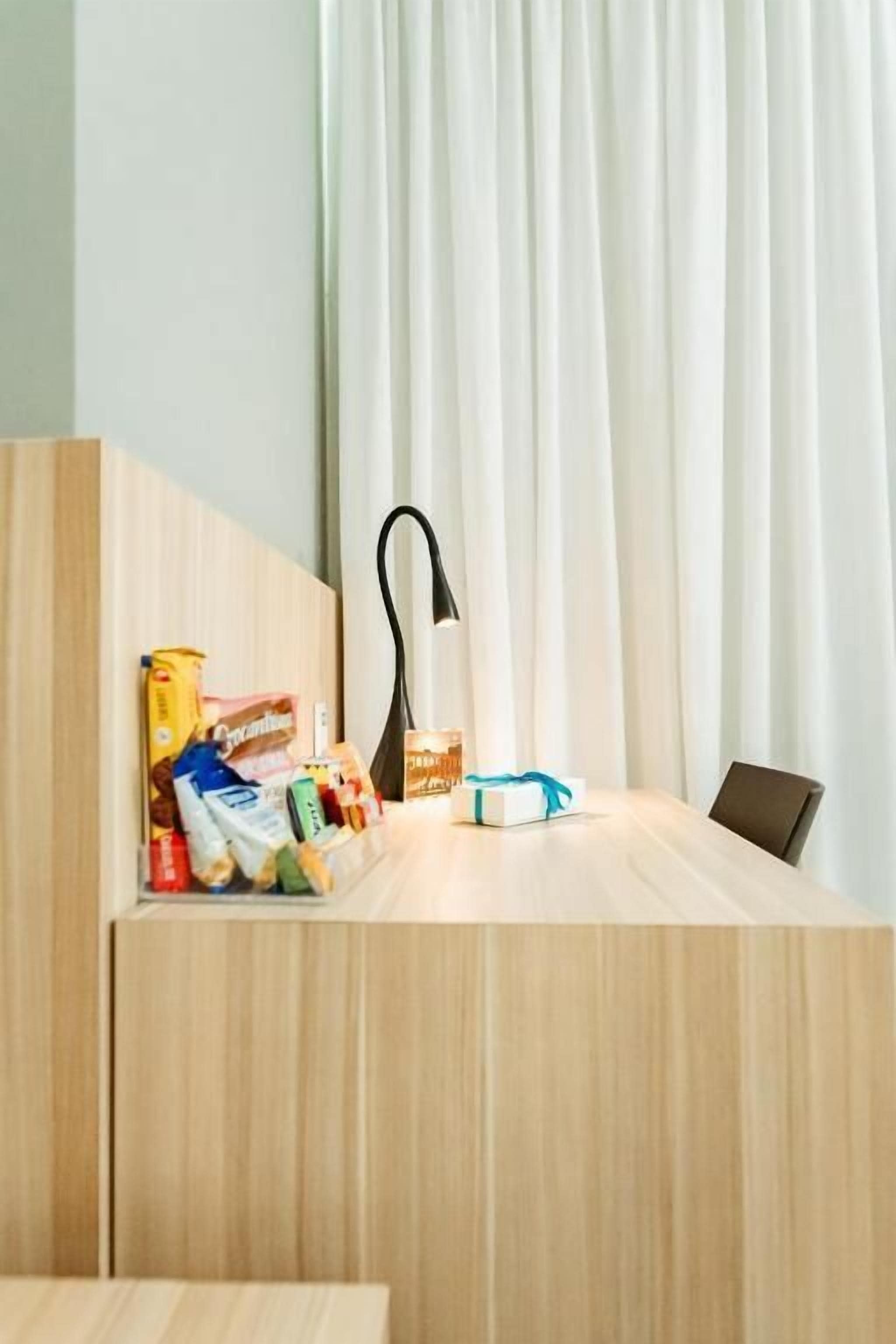 Een houten bureau met een lamp, een klein cadeautje en verschillende lekkernijen.