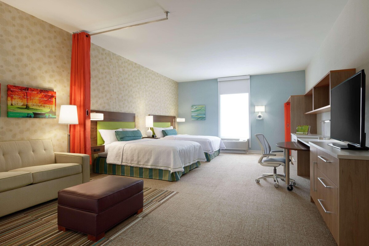 Habitación de hotel con sofá, dos camas, escritorio, televisor y ventana.