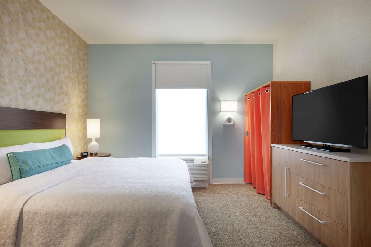 Una habitación de hotel con una cama, televisión, armario y ventana.