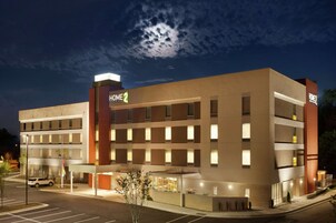 A multi-story hotel with a modern design, featuring a prominent "HOME2" sign, a covered entrance, and a parking lot.