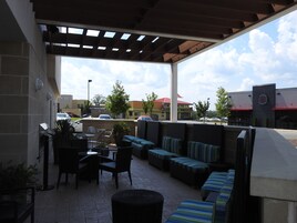 An outdoor patio with seating and a grill area, overlooking a parking lot and buildings.