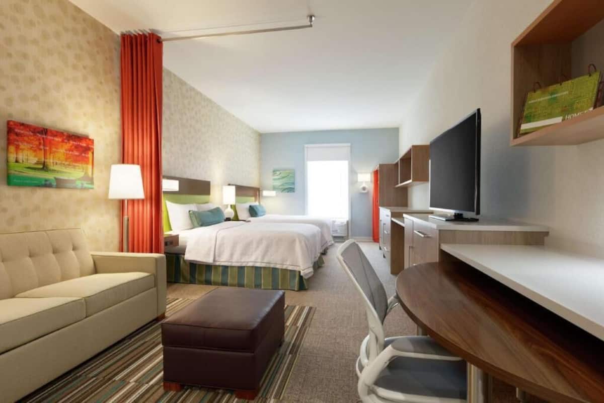 A hotel room with a bed, a sofa, a desk, a TV, and a painting on the wall.