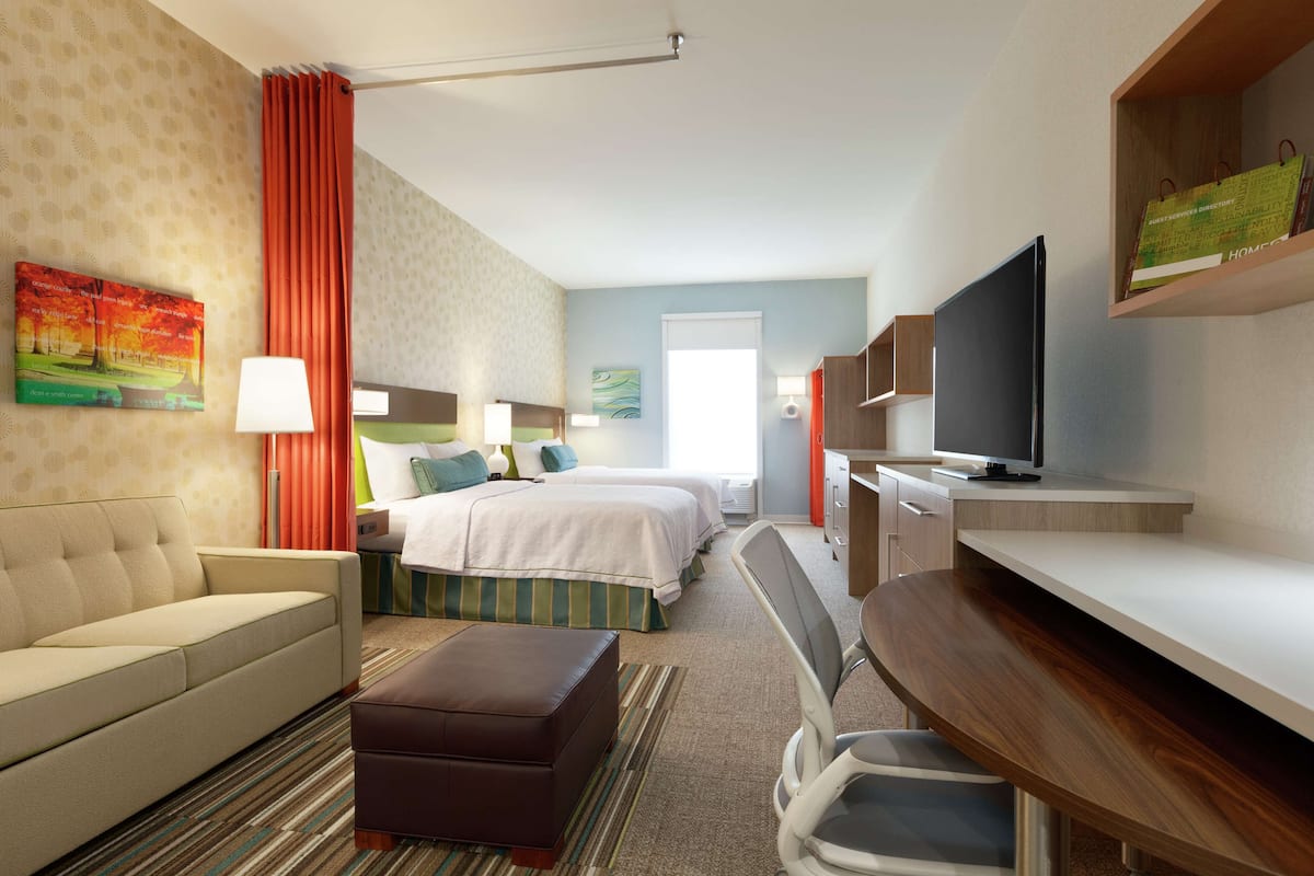 A hotel room with a bed, a sofa, a desk, a television, and a painting on the wall.