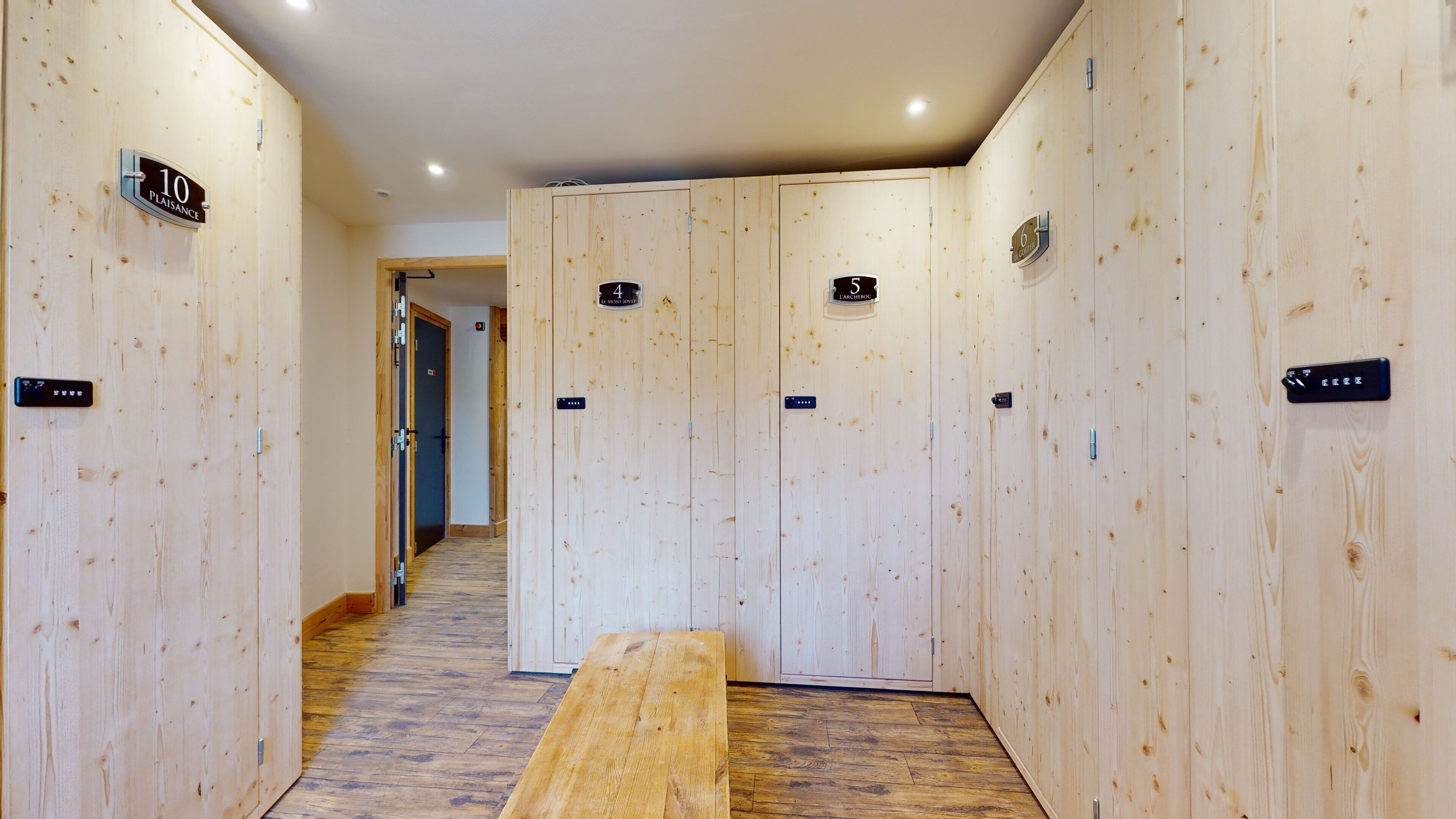 Un couloir avec des casiers en bois numérotés de 1 à 10, un banc et une porte portant l’inscription « 10, place de la Plaisance ».