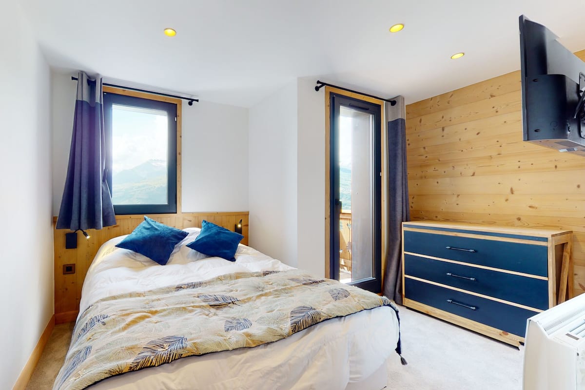 A bedroom with a bed, a wooden wardrobe, and a window with curtains.