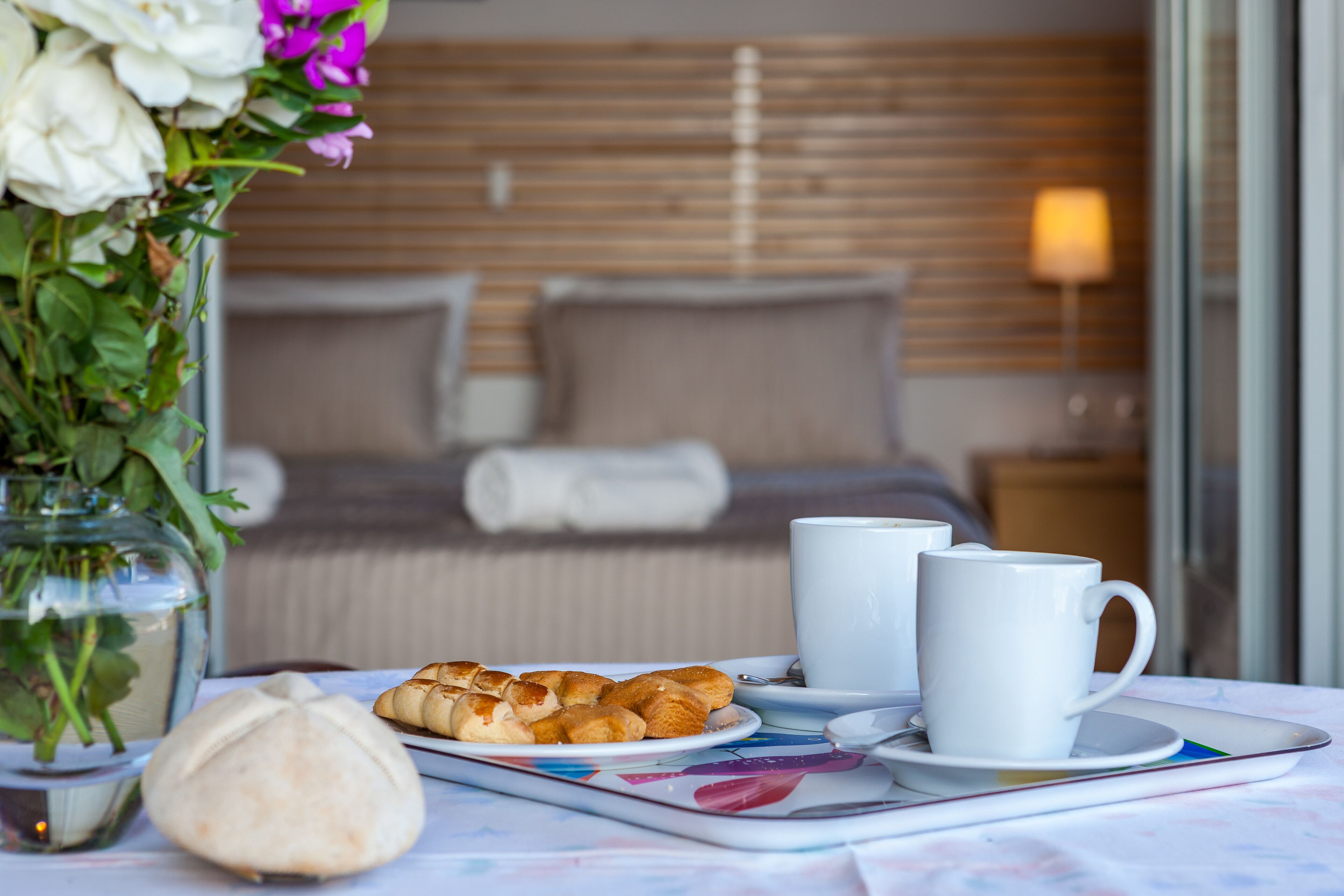 A neatly arranged breakfast table with pastries, two white cups, and a small vase of flowers.
