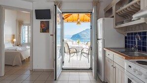 Una cocina con vista al mar, un comedor con mesa y sillas, y un dormitorio con cama y cortinas.