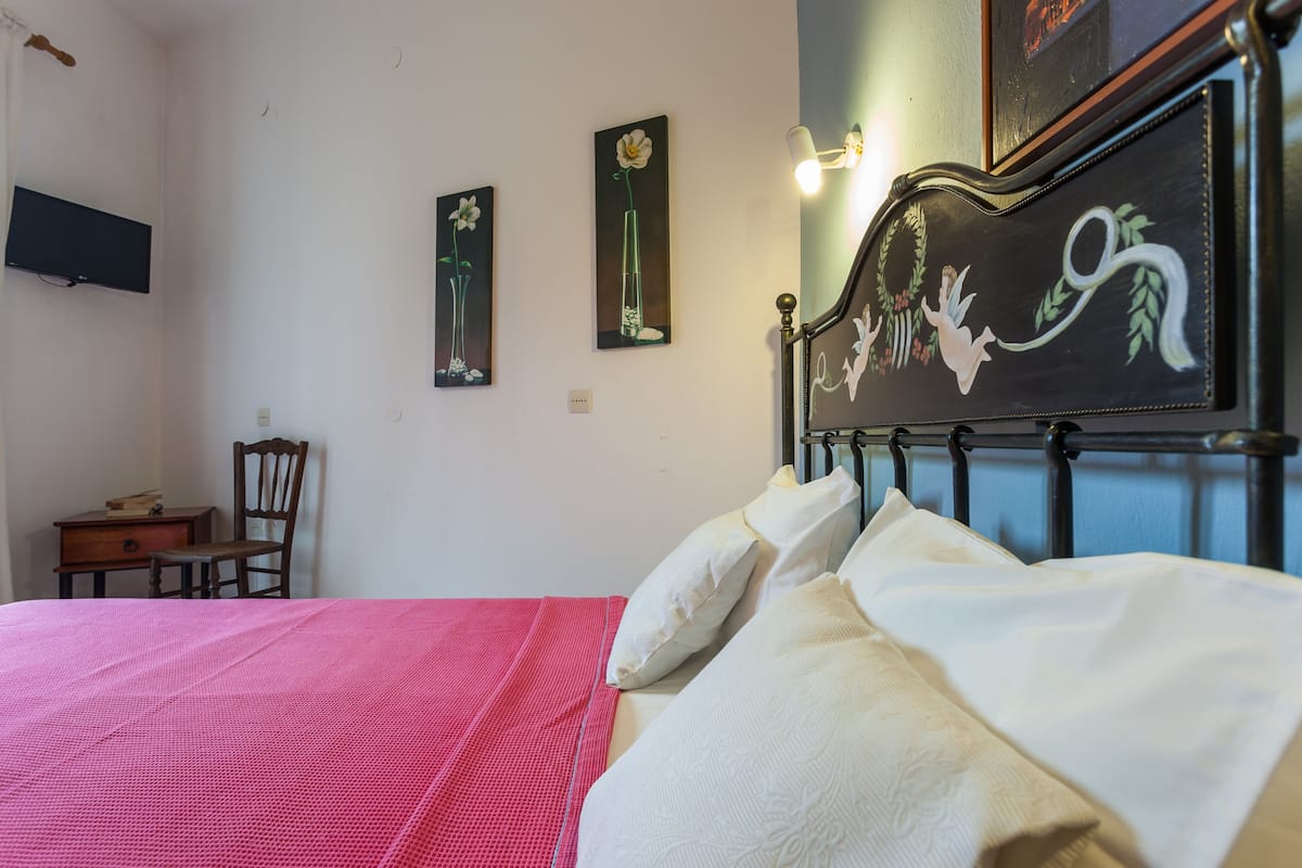 Une chambre à coucher comprenant un lit, des oreillers, une chaise, une commode et des œuvres d’art accrochées au mur.