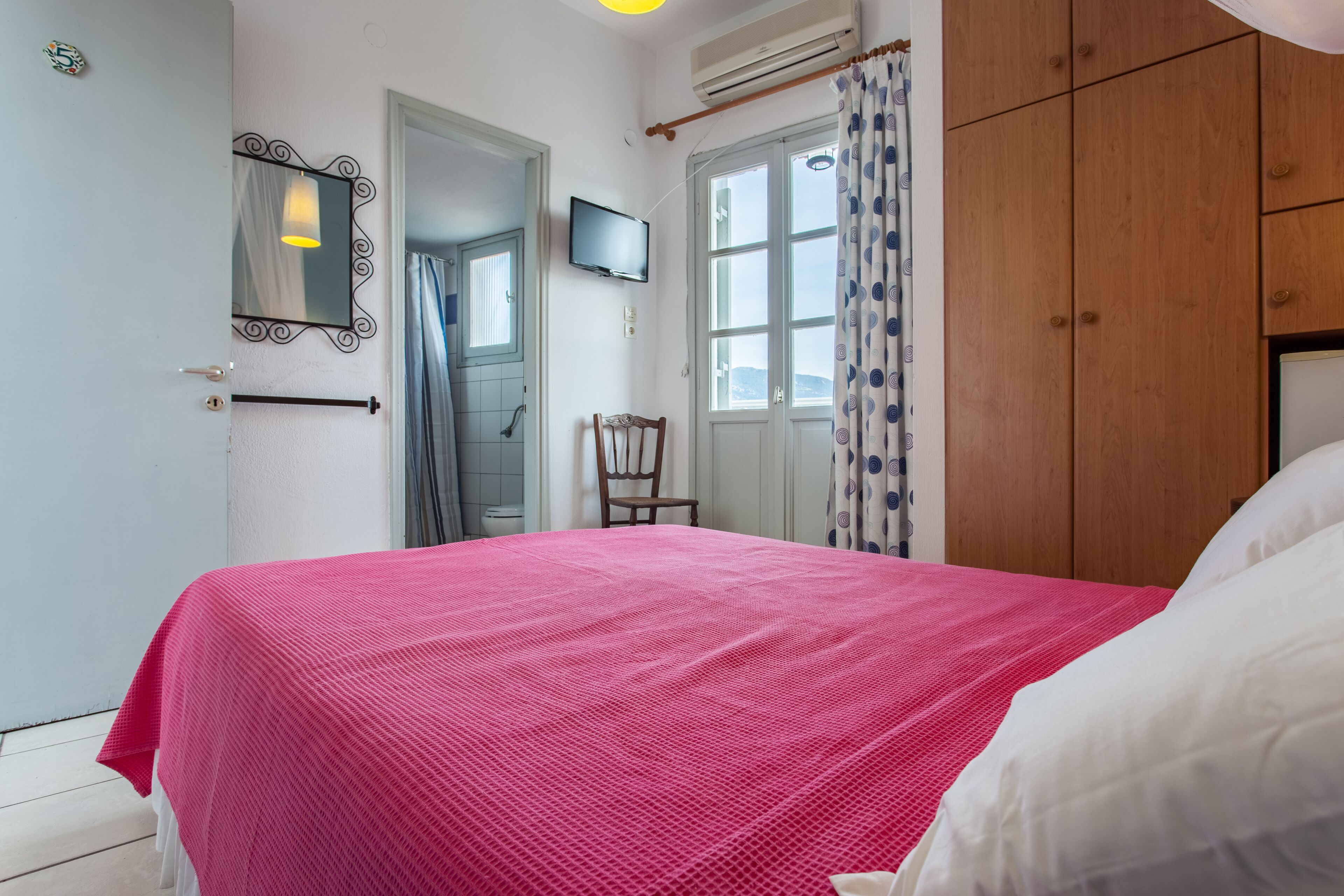 A bedroom with a bed, a wooden wardrobe, a television, and a mirror on the wall.