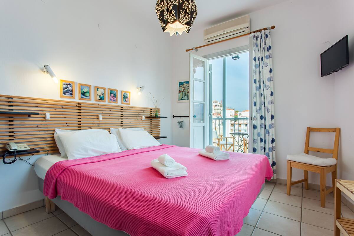 Une chambre avec un lit, une chaise, une télévision et un balcon offrant une vue.
