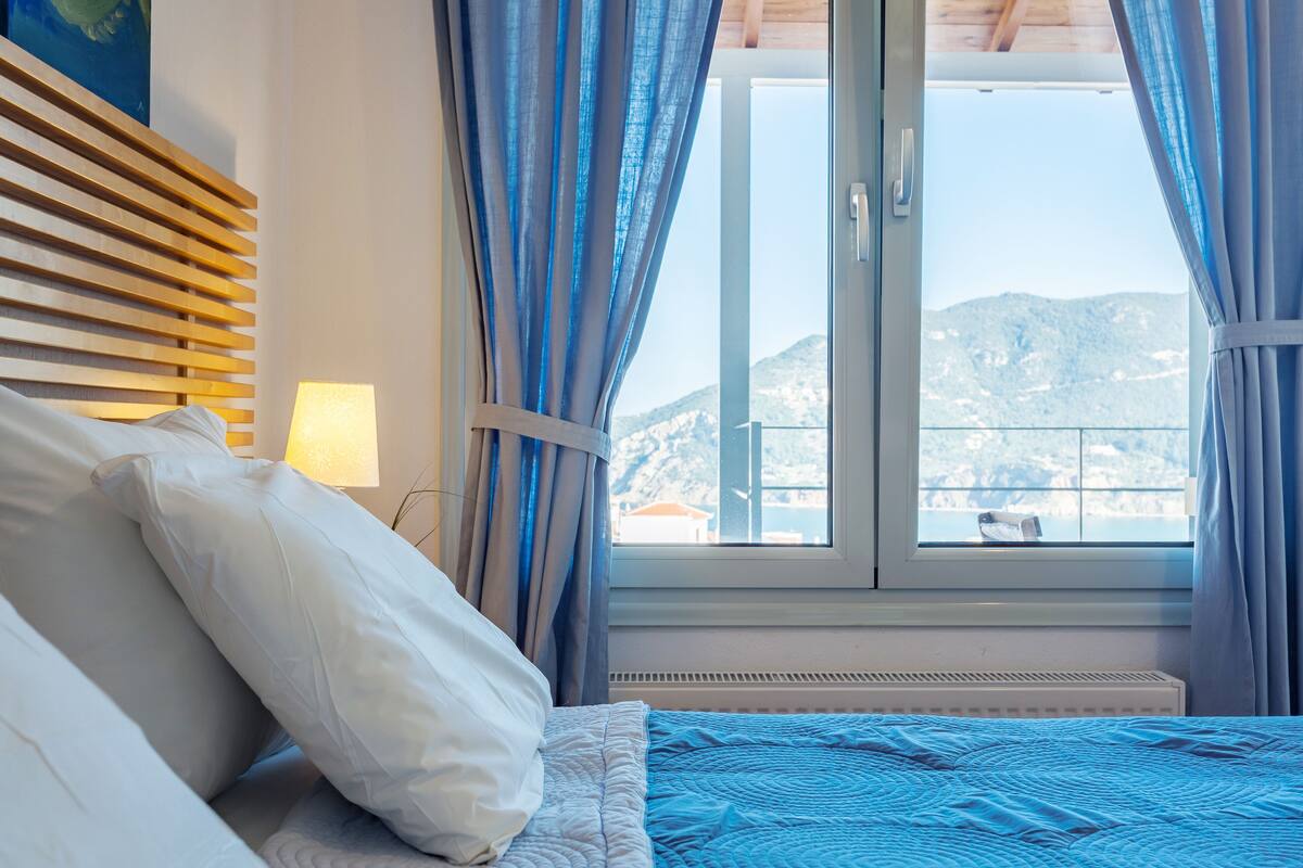 Une chambre à coucher avec un lit, une fenêtre avec des rideaux, une lampe et une vue sur les montagnes.
