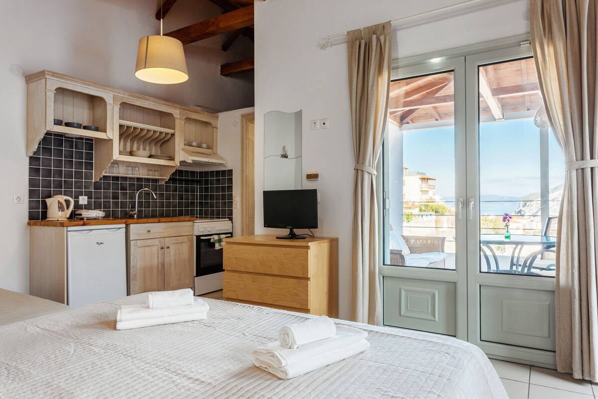 Une chambre d’hôtel comprenant un lit, une kitchenette, une télévision et un balcon avec des rideaux.