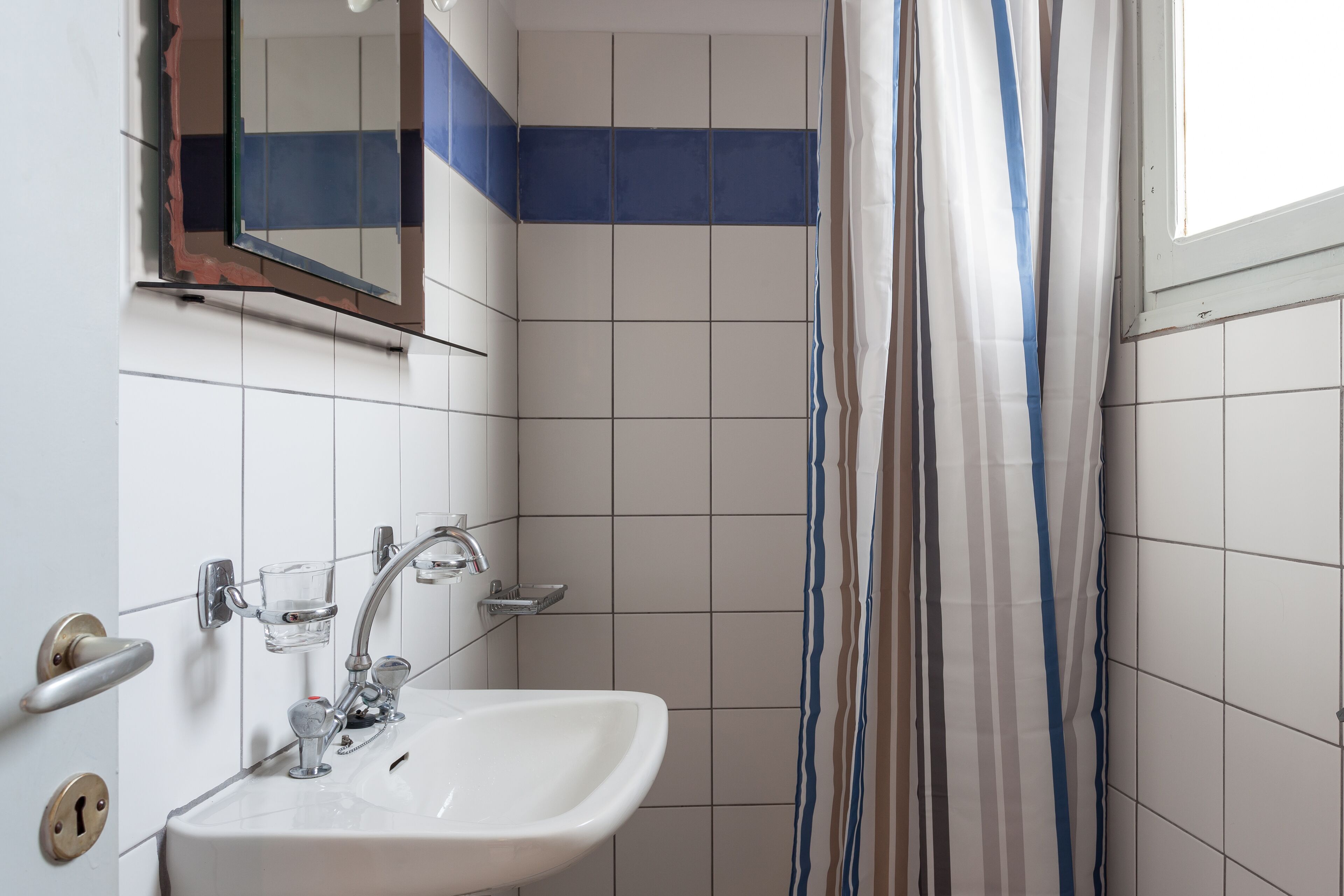 A bathroom with a sink, mirror, and striped shower curtain.