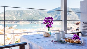 Un balcón con una mesa dispuesta para el desayuno, con vistas a un pueblo costero y montañas.