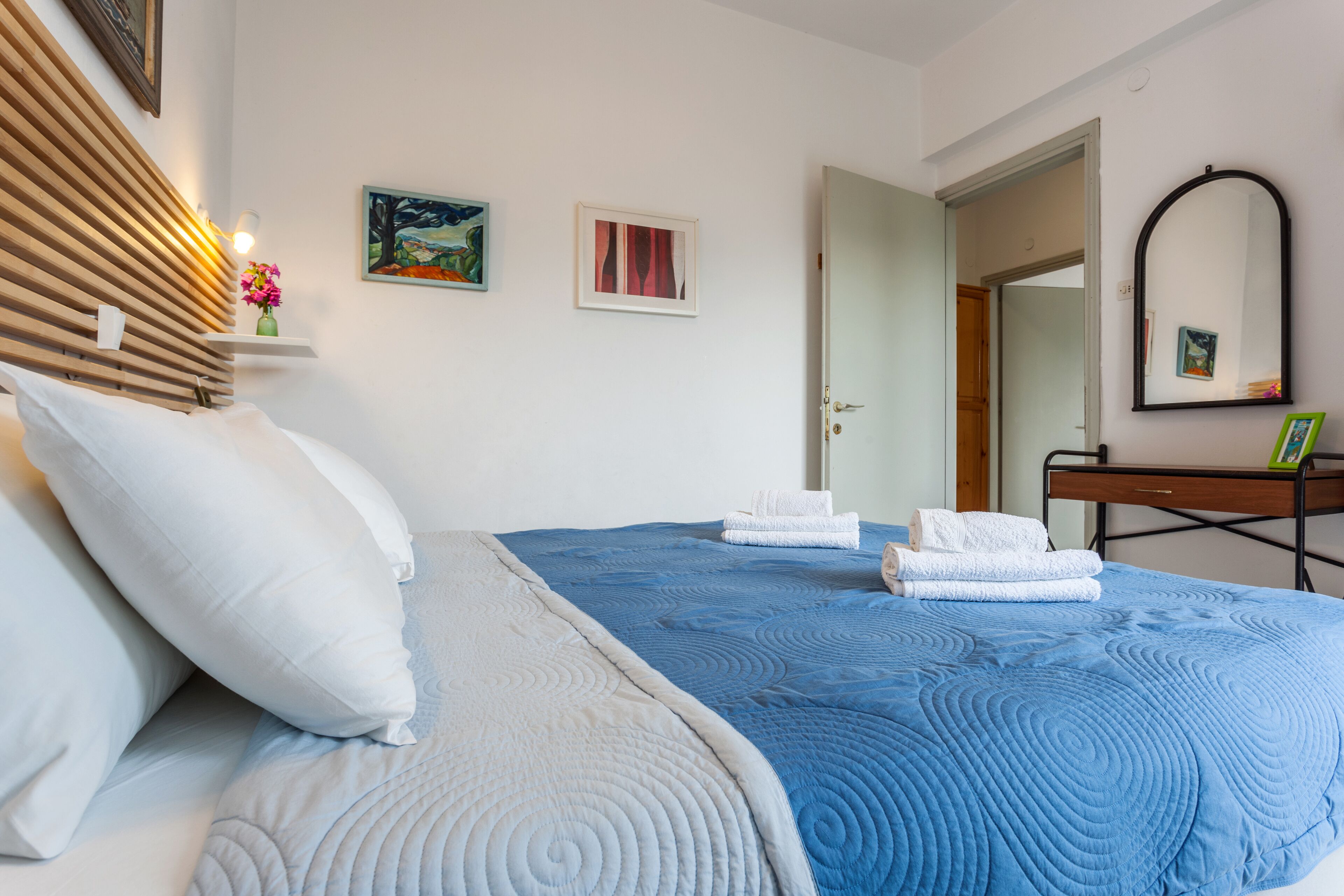 Una cama bien hecha con colcha azul, almohadas blancas y toallas dobladas con cuidado.