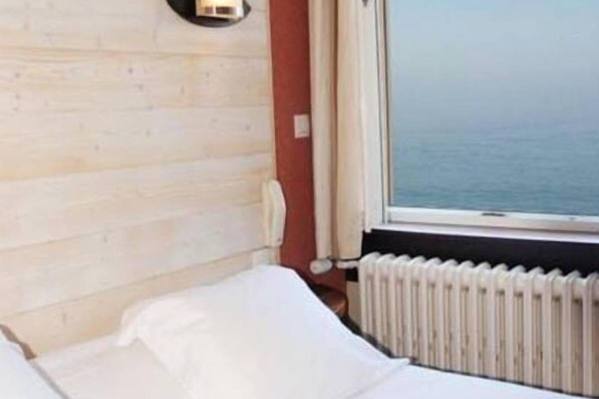 A hotel room with a wooden headboard, a window with a view of the sea, and a white bed.