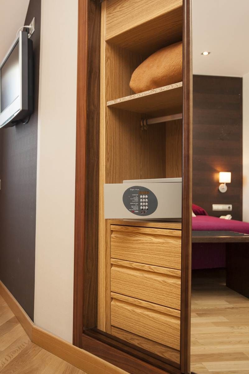 A wooden wardrobe with a control panel, a television mounted on the wall, and a bed with a purple blanket.