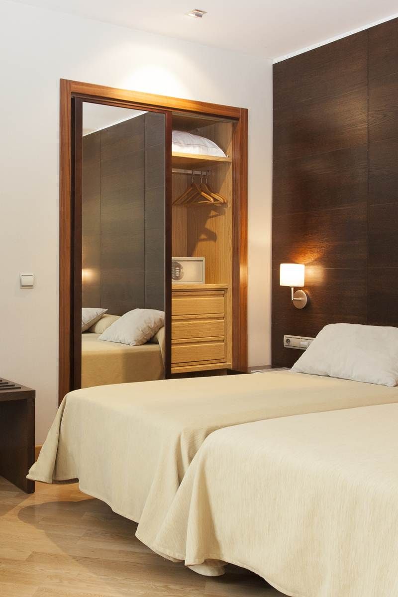 Habitación de hotel con cama, armario de madera, mesita de noche y lámpara de pared.