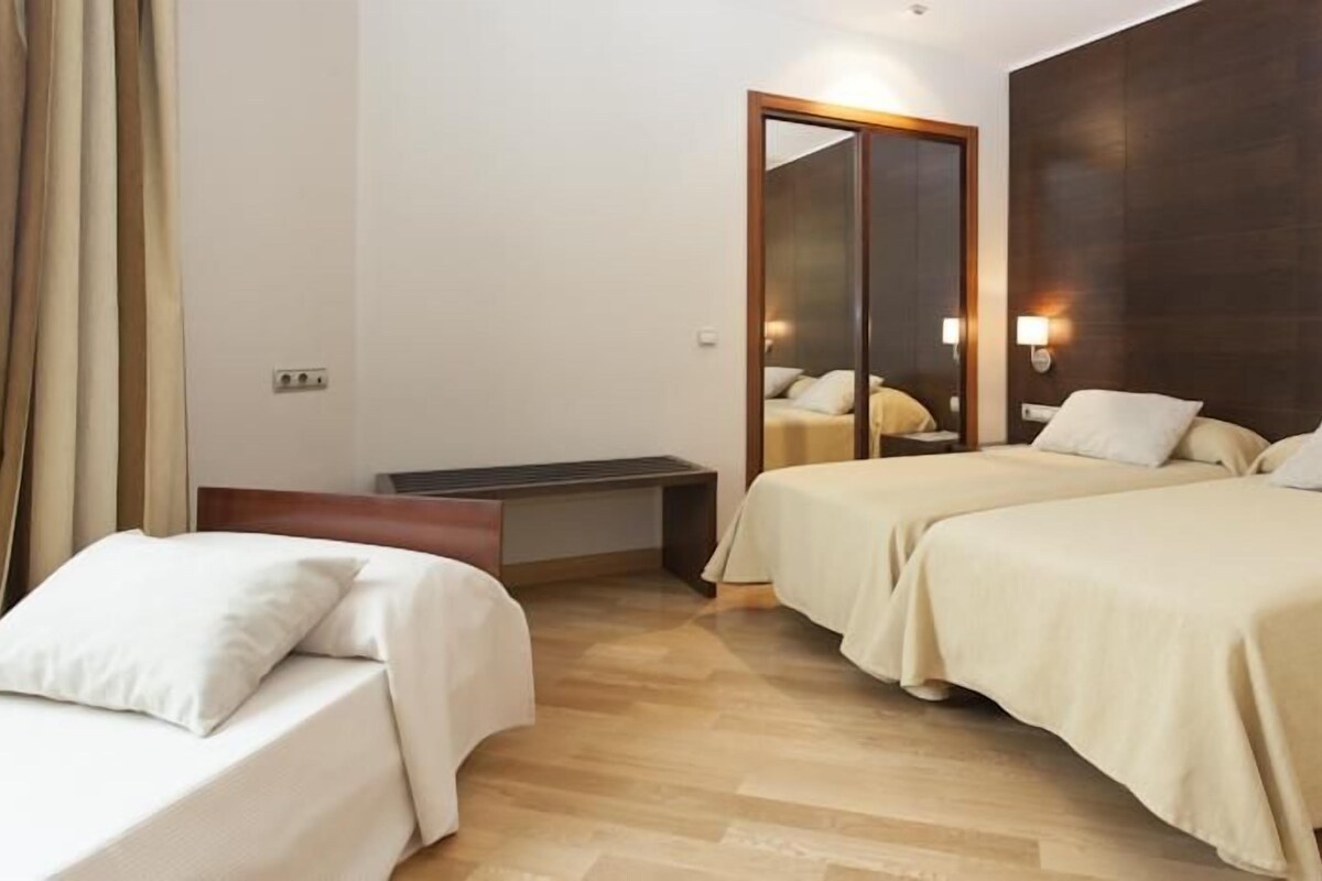 Une chambre d’hôtel avec deux lits, une tête de lit en bois, une table de chevet, un miroir et un luminaire.