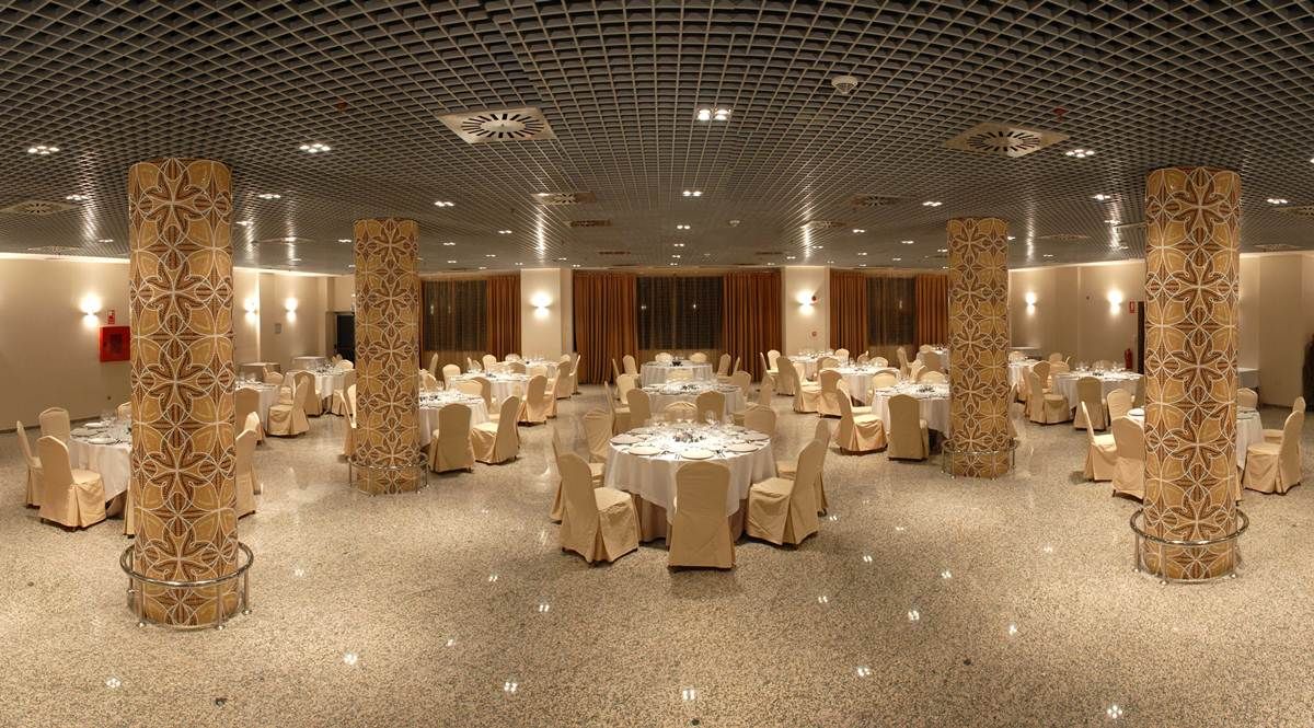 A banquet hall with round tables and chairs, decorative pillars, and a ceiling with a grid pattern.