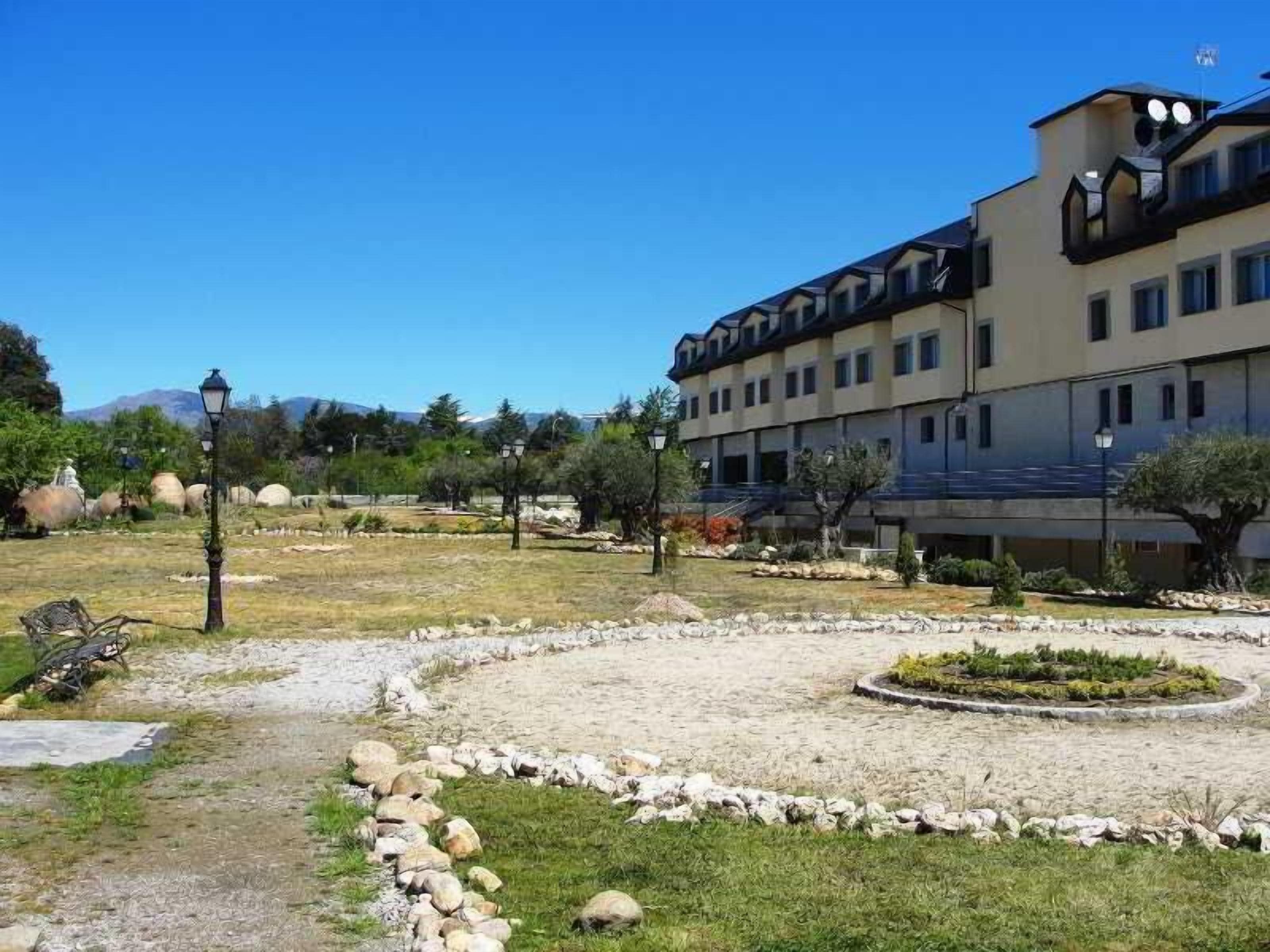 Hotel d'estil arquitectònic modern, amb teulada plana i nombroses finestres. A l'entorn, un jardí paisatge amb una llera circular de flors i un camí de grava.