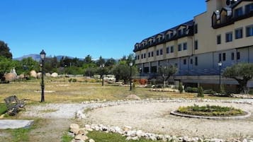 Hotel d'estil arquitectònic modern, amb teulada plana i nombroses finestres. A l'entorn, un jardí paisatge amb una llera circular de flors i un camí de grava.
