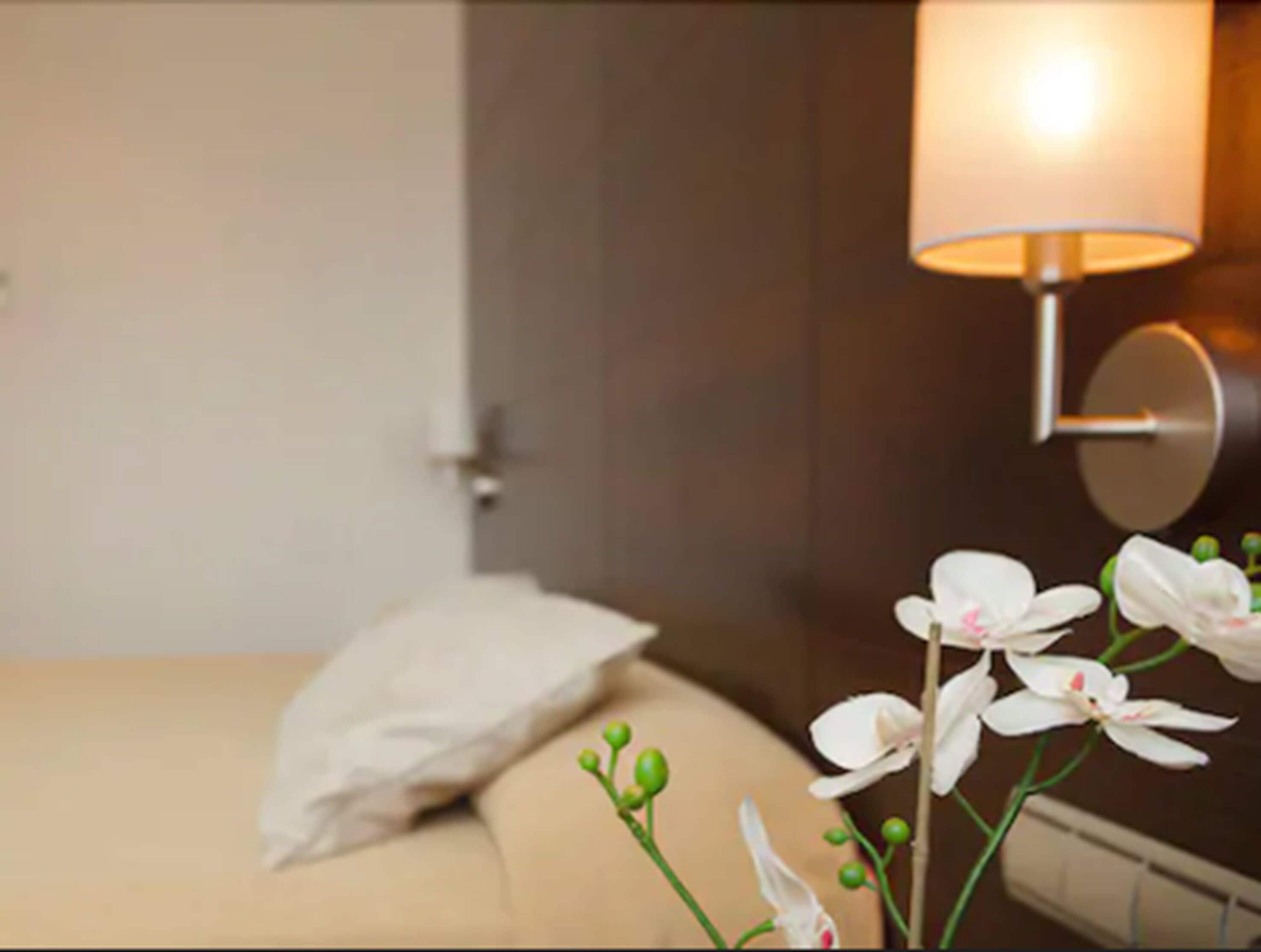 Une chambre d’hôtel avec un lit, une table de chevet et une lampe fixée au mur.