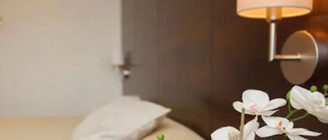 A hotel room with a bed, a nightstand, and a wall-mounted lamp.