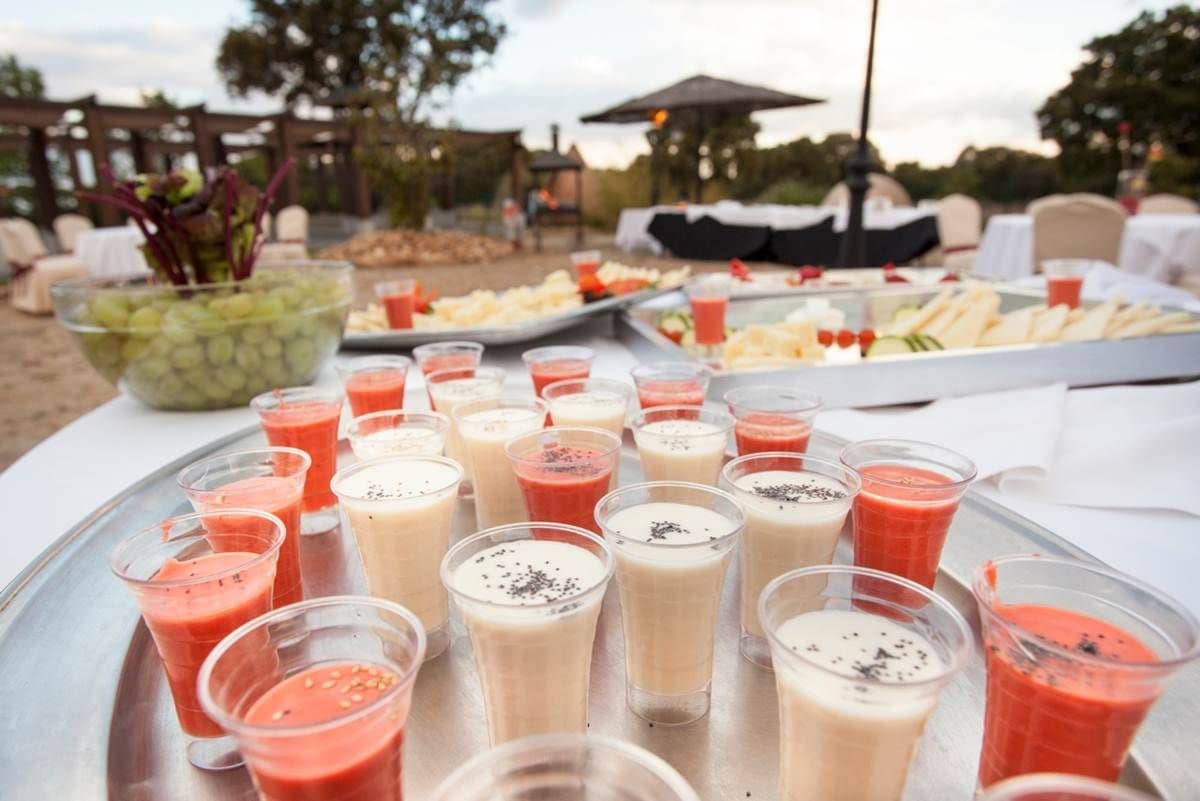 Una mesa de buffet con diversos alimentos y bebidas, incluyendo un bol grande de uvas y una bandeja de queso y galletas.