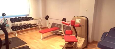 A gym with exercise equipment including a treadmill, bench, and weight machines.