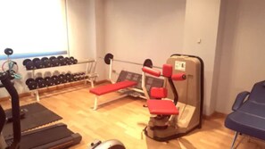 Ein Fitnessraum mit Trainingsgeräten, darunter Laufband, Bank und Kraftgeräte.