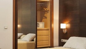 A hotel room with a bed, a wooden wardrobe, a nightstand, and a wall-mounted lamp. - FC Villalba (Collado Villalba)