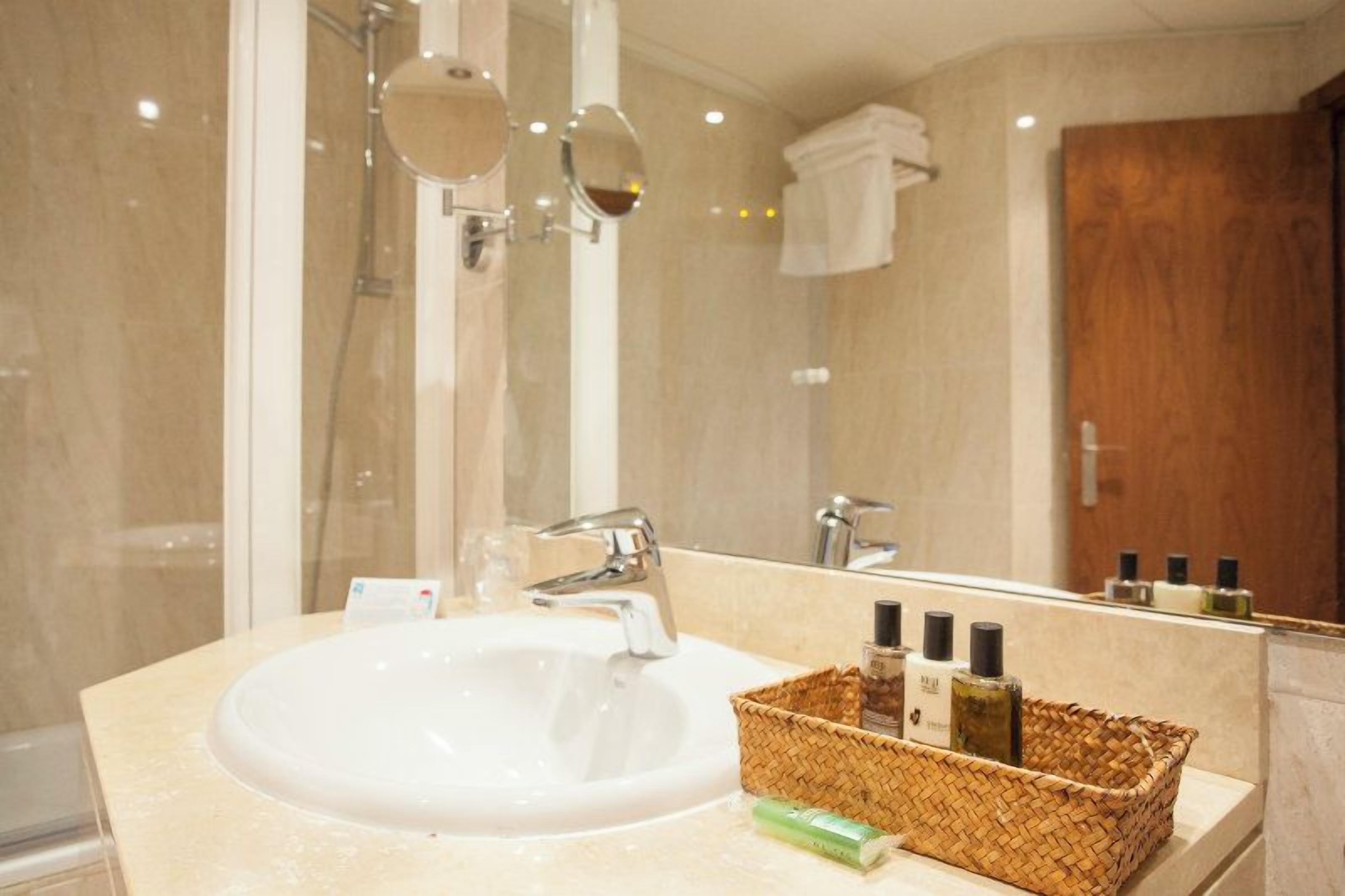 Un baño con lavamanos blanco, un espejo y una puerta de madera.