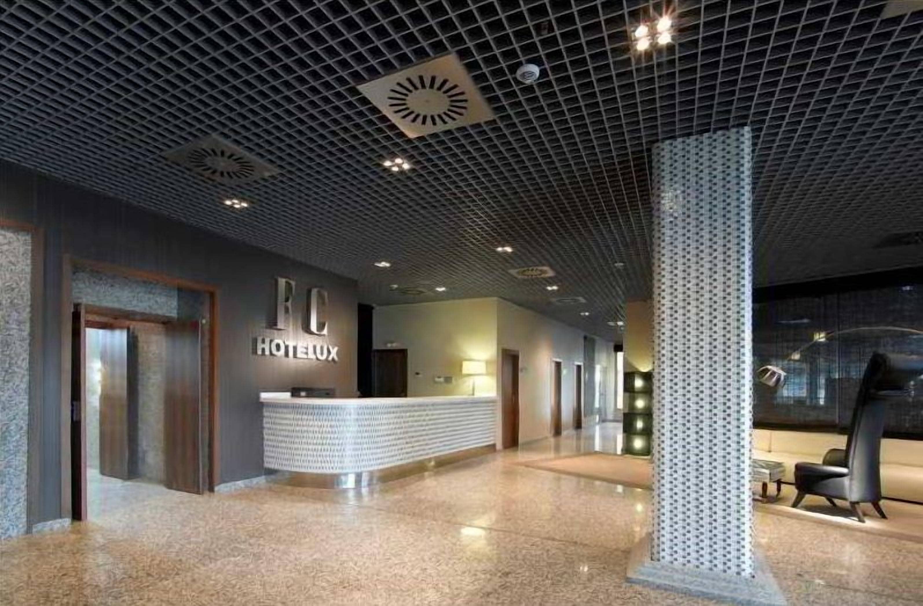 A modern hotel lobby with a reception desk, a large pillar, and a seating area.