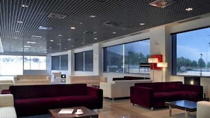 A modern hotel lobby with a high ceiling, large windows, and a mix of seating areas including sofas and armchairs. - FC Villalba (Collado Villalba)