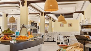 Een buffetgedeelte met diverse etenswaren, waaronder fruit en brood, en een zithoek met witte stoelen.