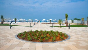 Een promenade aan het strand met ligbedden en parasols, palmbomen en een helder uitzicht op de oceaan.