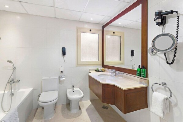A modern bathroom with a bathtub, toilet, bidet, vanity with a mirror, and a hairdryer mounted on the wall. - Al Hamra Palace Beach Resort (Ras al Khaimah)