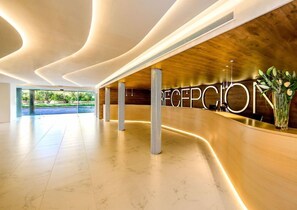 A modern reception area with a curved reception desk, a large reception sign, and a view of the outdoors. - Hotel Carlos L (Benidorm)