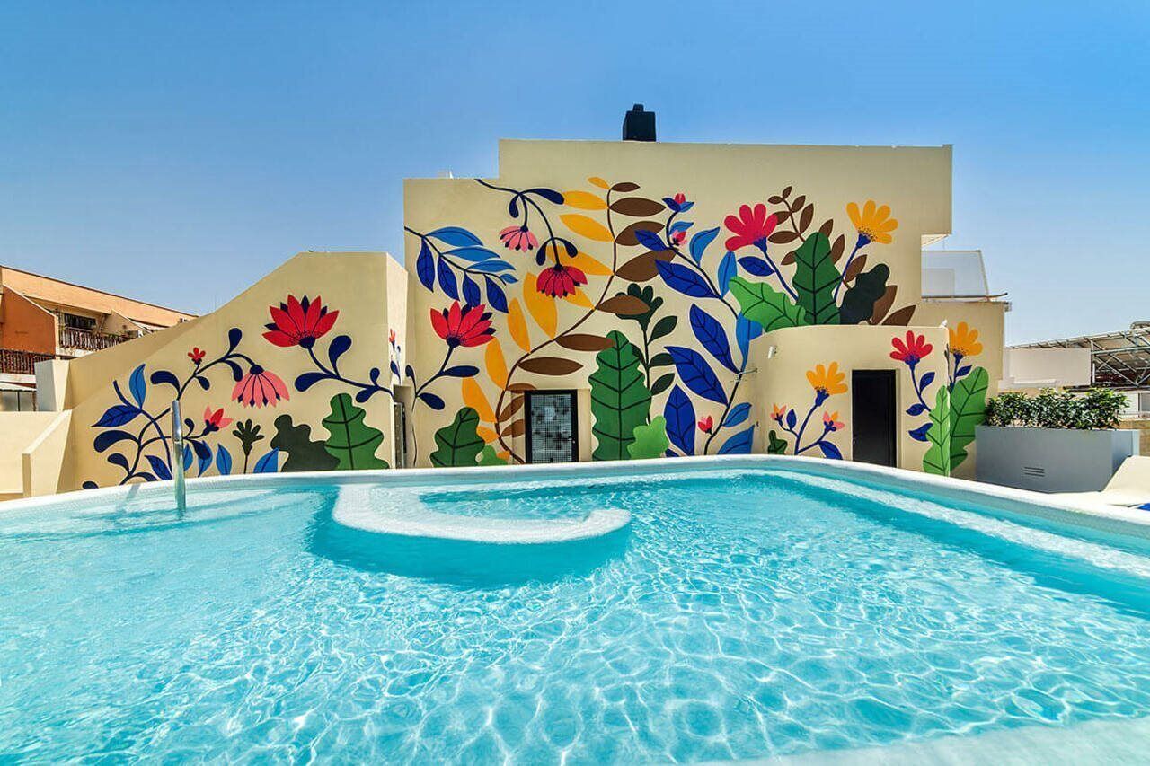 Una piscina con un mural colorido de flores y hojas en la pared contigua.
