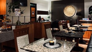 A modern restaurant with a long counter, multiple tables, and chairs. There is a buffet area with food and drinks, and a large wall-mounted light fixture. - Hotel Prinz (Munich)