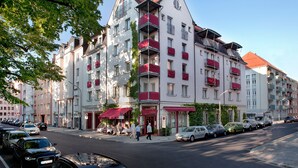 A multi-story hotel with balconies, a restaurant on the ground floor, and a row of parked cars along the street. - Hotel Prinz (Munich)