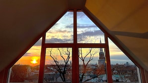 A view from a room with a large window, featuring a cityscape with buildings and a tower, during sunset. - Hotel Prinz (Munich)