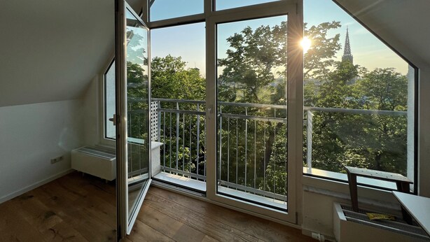 A room with large windows, a wooden floor, and a view of trees and a tower. - Hotel Prinz (Munich)