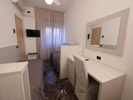 Una camera d'albergo con un letto, una scrivania, una sedia, una televisione e una finestra con tende.