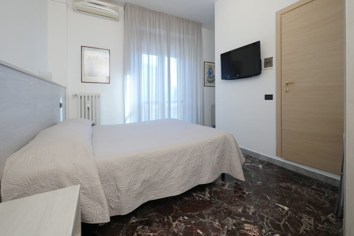 A hotel room with a bed, a television, a door, and a radiator.