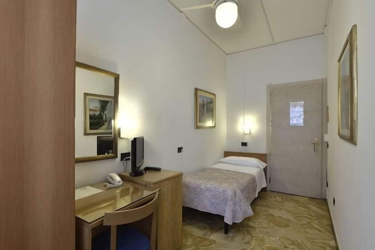 A hotel room with a bed, a desk with a telephone, a chair, and a door.