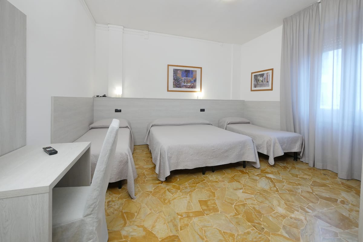 A hotel room with two single beds, a small desk, a telephone, and a window with curtains.