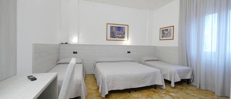 A hotel room with two single beds, a small desk, a telephone, and a window with curtains.